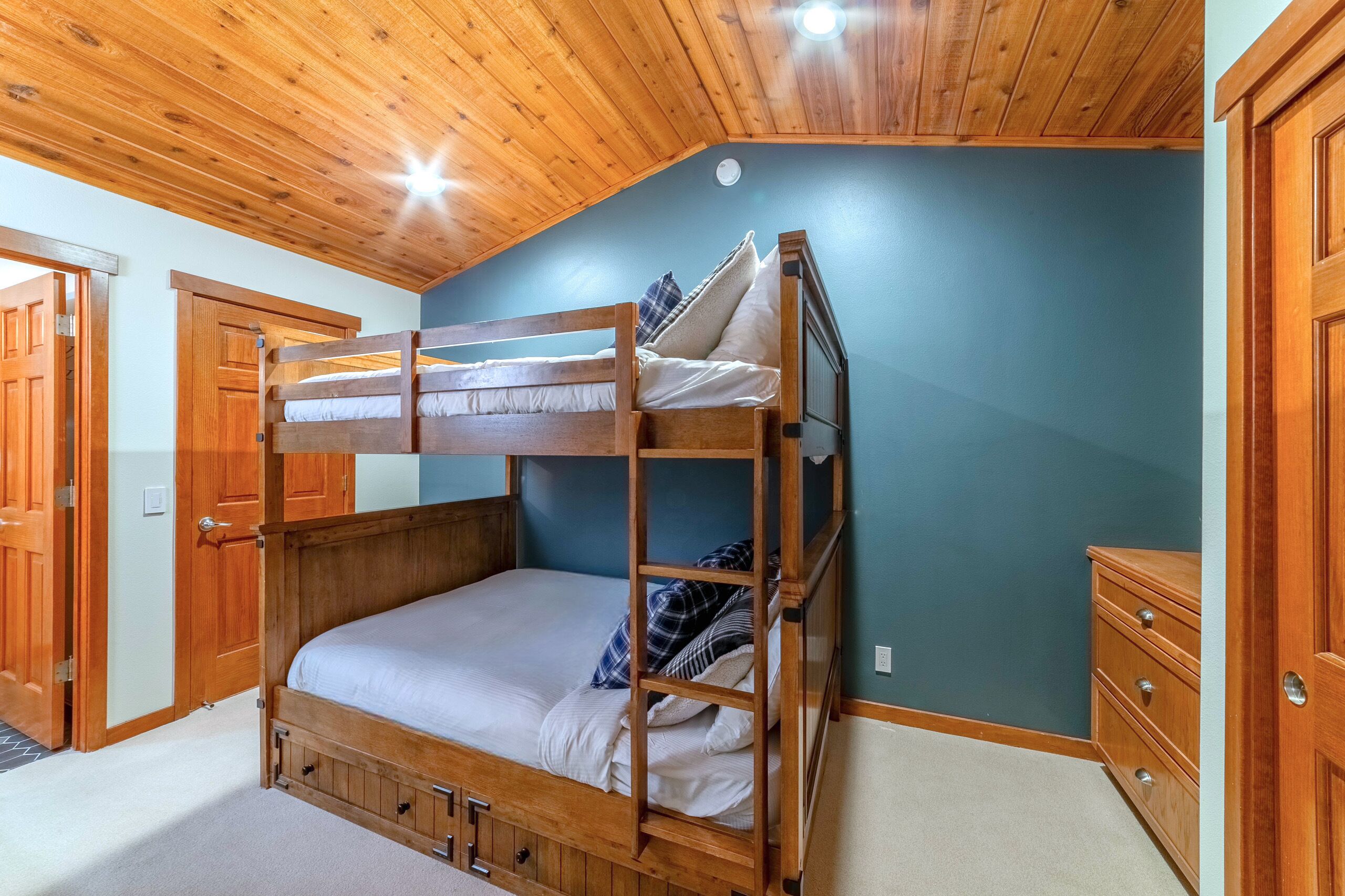 Une chambre avec un lit superposé, des murs et un plafond en bois, une commode et une porte.