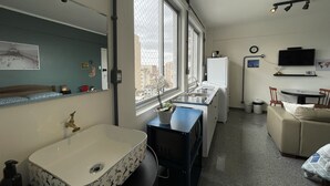 Una camera d'albergo compatta con un'ampia finestra, un lavandino, un angolo cottura, un divano e una TV a parete.