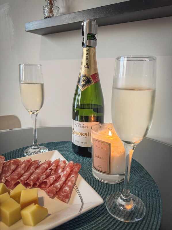 A table with a bottle of Cuvée Classico wine, a candle, a glass of white wine, and a plate of cured meats and cheese.