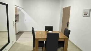 Zona pranzo con tavolo e sedie in legno, soffitto a travi a vista e una porta sulla destra.