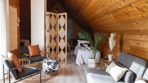 A cozy loft bedroom with a sloped ceiling, a bed, a seating area with a sofa and chairs, and a large window allowing natural light. - #Slowtravel+Wellness~woodfired hot tub, cold plunge, sauna, forestbathing, beach (Halfmoon Bay)