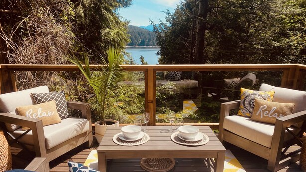 A deck with two sofas, a coffee table, and a view of a lake. - #Slowtravel+Wellness~woodfired hot tub, cold plunge, sauna, forestbathing, beach (Halfmoon Bay)