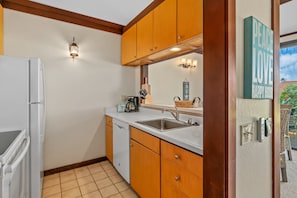 Kitchen area with refrigerator, dishwasher, and sink, featuring a light fixture and decorative sign.