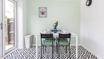 A dining area with a white table, two chairs, a vase with flowers, and a clock on the wall.