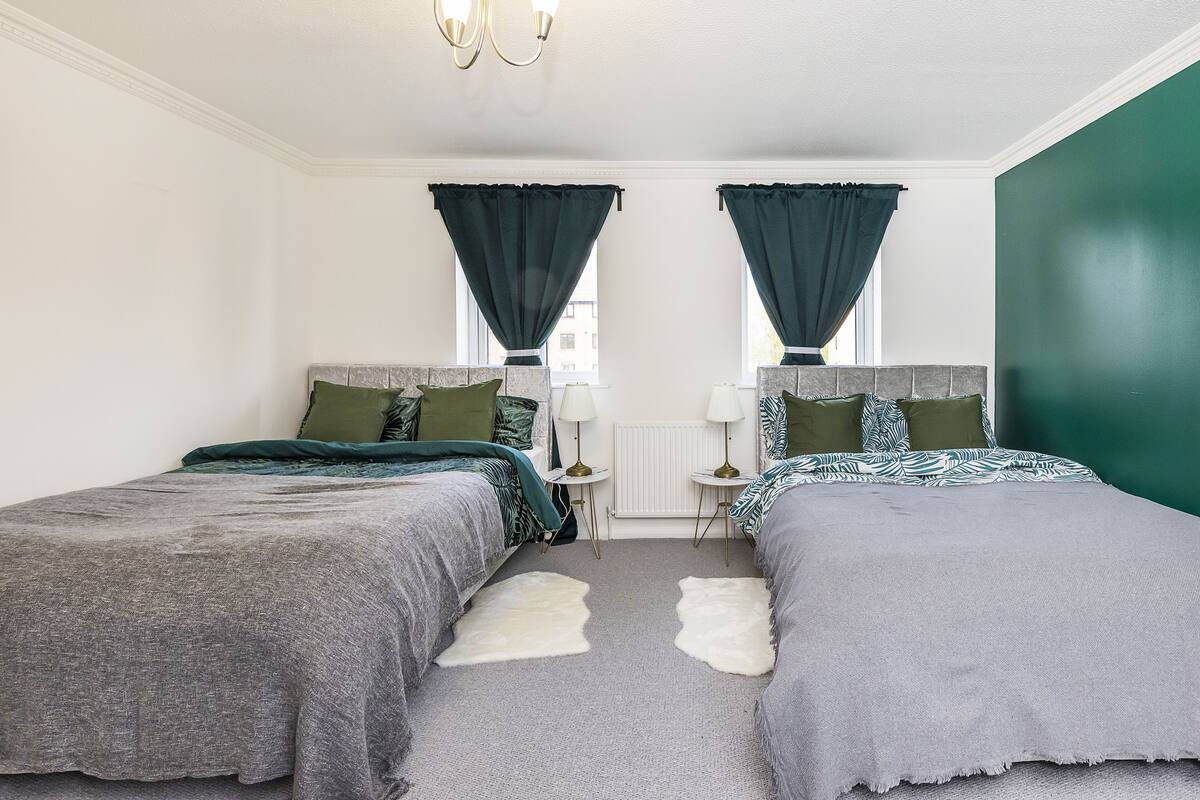 A bedroom with two beds, a small table, and a window with curtains.