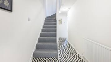 A staircase with a geometric patterned floor, white walls, and a framed picture on the left.