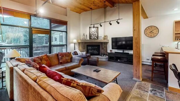 Una amplia sala de estar con chimenea, televisor y comedor con mostrador de cocina.