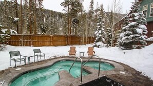 Un jacuzzi rodeado de árboles cubiertos de nieve y una valla de madera.