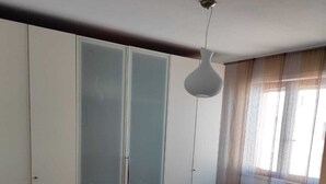 Ein Schlafzimmer mit Bett, Kleiderschrank, Deckenleuchte und Fenster.