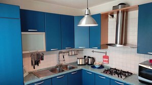 Eine moderne Küche mit blauen Schränken, einer Edelstahl-Spüle, einem Gasherd und einer hängenden Pendelleuchte.