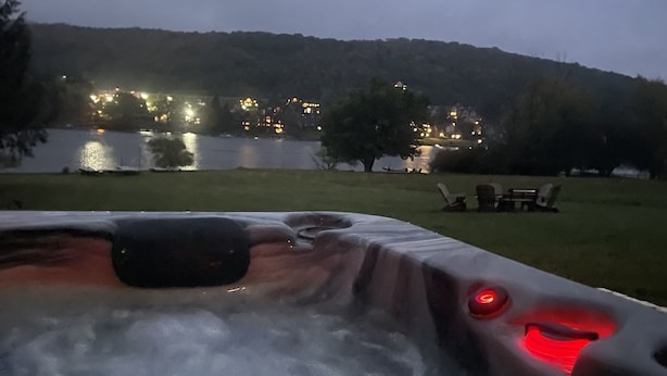 Uma banheira de hidromassagem com vista para um lago e um edifício iluminado ao fundo.
