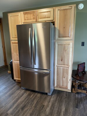 A stainless steel refrigerator in a kitchen with wooden cabinetry and a dark wood floor.