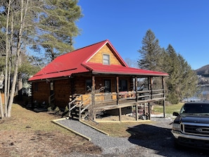 A log cabin with a red roof, a porch, and a gravel driveway.