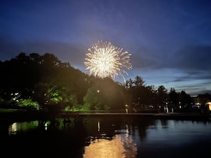 A nighttime view of a fireworks display over a body of water with trees and a bridge in the foreground.