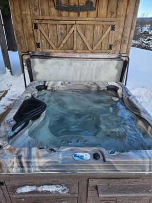 A hot tub with a wooden exterior and a metal lid, surrounded by snow. - Private Home, Dock, Hot Tub, Lakefront, Large yard (McHenry)