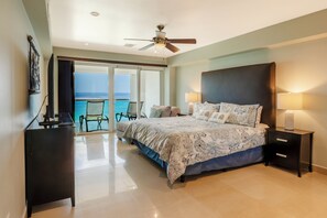 A hotel room with a bed, a desk, a chair, a ceiling fan, and a view of the ocean. - CASA MERMAID - Newly Redecorated Condo On The 6th Floor (Cozumel)