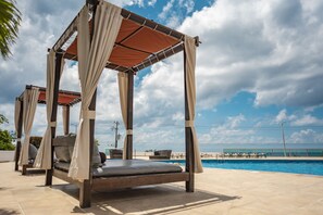Un espacio de estar techado al aire libre con piscina al fondo.