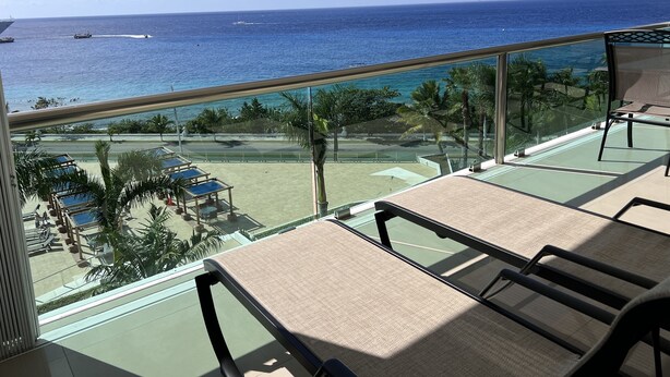 A balcony with a view of the ocean and a pool area with lounge chairs.