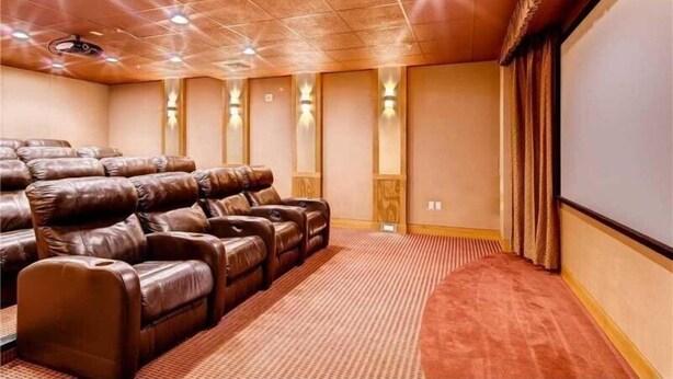 Une salle de cinéma privée avec des fauteuils inclinables en cuir, un sol recouvert de moquette et un grand écran mural.