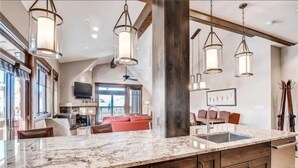 A spacious kitchen with a large marble countertop, wooden cabinets, and pendant lighting. - Luxury 4 Bedroom Penthouse Rental off Main Street Within Walking Distance to Peak 9 (Breckenridge)
