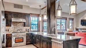 A spacious kitchen with dark wood cabinets, a large island, and a stone backsplash. - Luxury 4 Bedroom Penthouse Rental off Main Street Within Walking Distance to Peak 9 (Breckenridge)