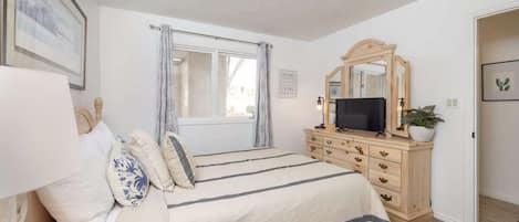 A bedroom with a bed, a dresser, a television, a window with curtains, and a mirror.