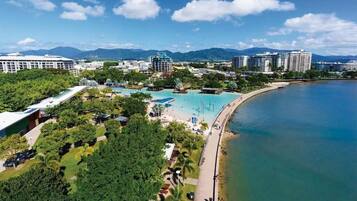 Vista aérea de un complejo turístico frente al mar, con una gran piscina y abundante vegetación.