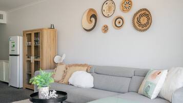 Una sala de estar con un sofá gris, un mueble de madera y decoración de arte tejido en la pared.