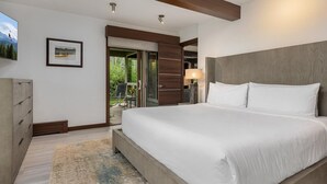 A modern bedroom with a large bed, wooden headboard, and a view of a balcony with outdoor furniture. - Warm and Cozy 3 Bedroom Ski In, Ski Out Condo in Snowmass Base Village (Snowmass Village)