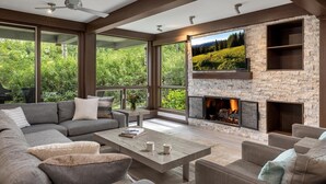 A modern living room with a stone fireplace, large windows, and a cozy seating area. - Warm and Cozy 3 Bedroom Ski In, Ski Out Condo in Snowmass Base Village (Snowmass Village)