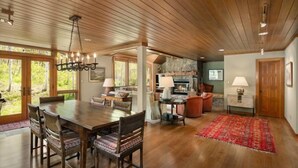 A spacious living area with a wooden ceiling, a dining table with chairs, a fireplace, and a red rug.