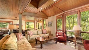 A spacious living room with a wooden ceiling, large windows, and a cozy seating area with a sofa and chairs.