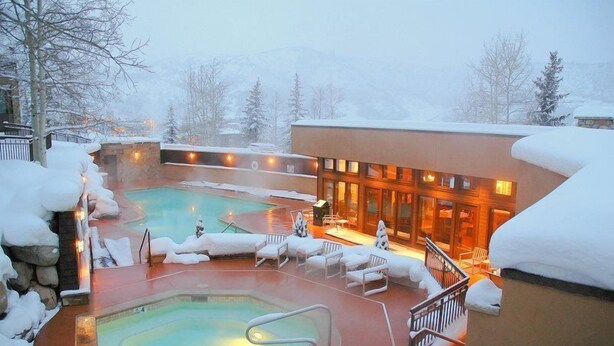 Ein mit Schnee bedeckter Poolbereich im Freien mit Liegestühlen und einem Gebäude mit großen Fenstern.