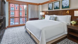 A hotel room with a large bed, a wooden headboard, a nightstand with a lamp, and a view of a red brick building through a large window. - Aspen St. Regis Luxury 3 Bedroom Residence - 5-star Resort in World Class Destination (Aspen)