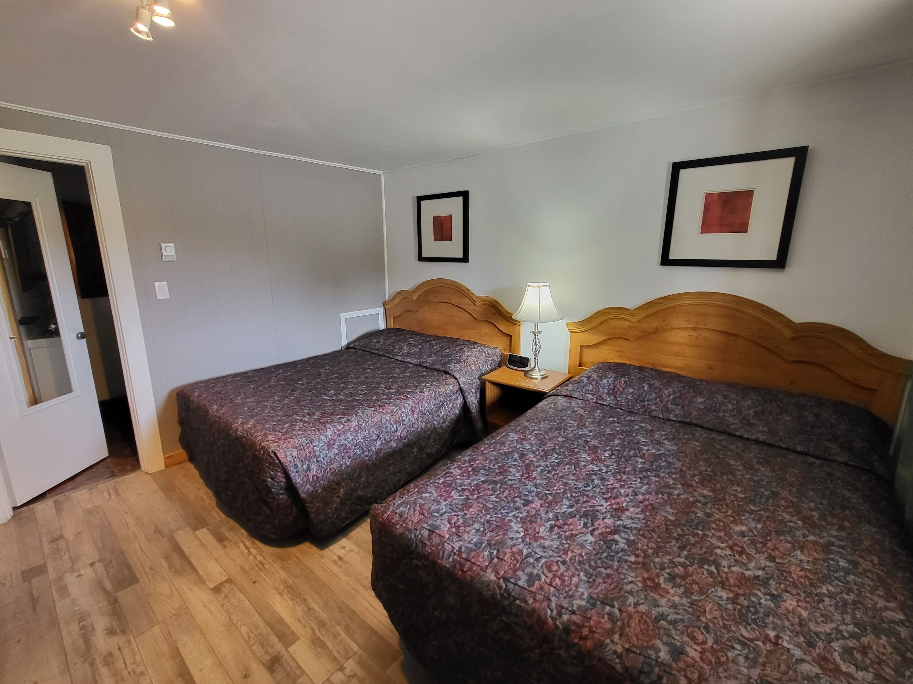 Habitación de hotel con dos camas, cabeceros de madera, una mesita de noche con lámpara y cuadros enmarcados en la pared.