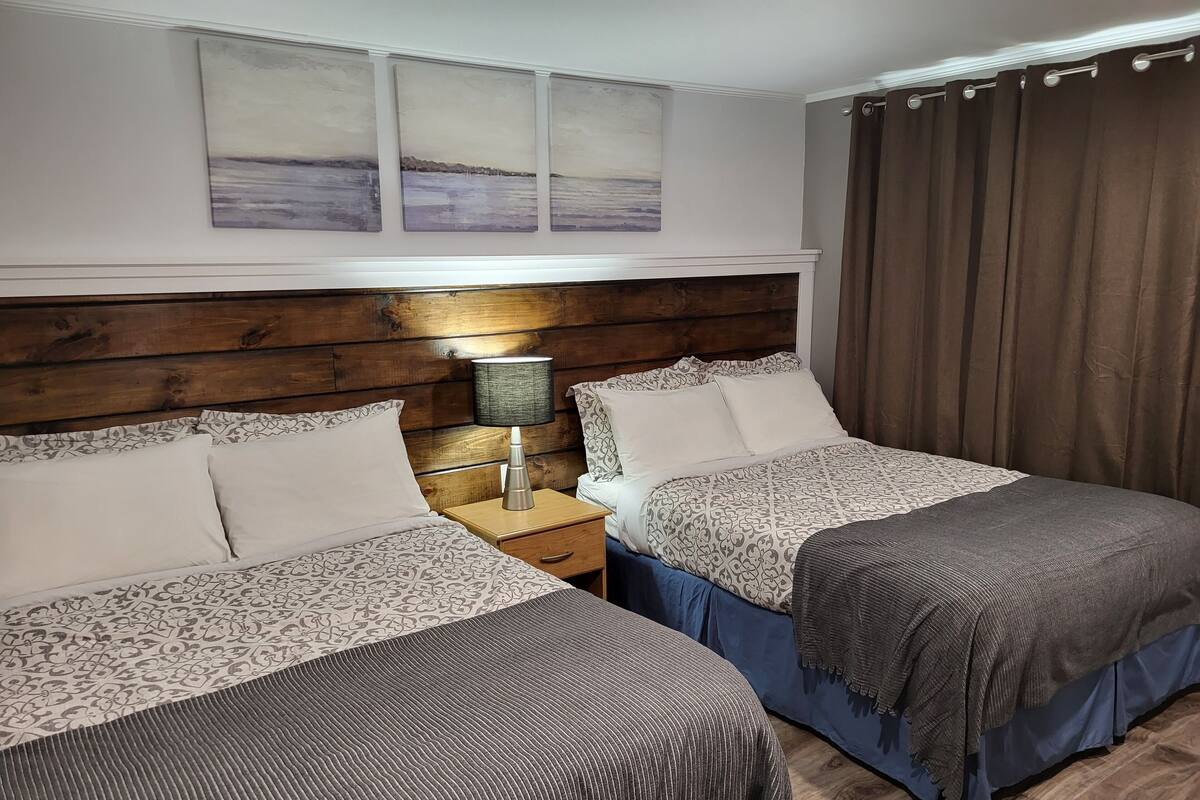 Habitació d'hotel amb dos llits, un capçal de llit de fusta, una meseta de nit amb una làmpada i vista al mar per la finestra.