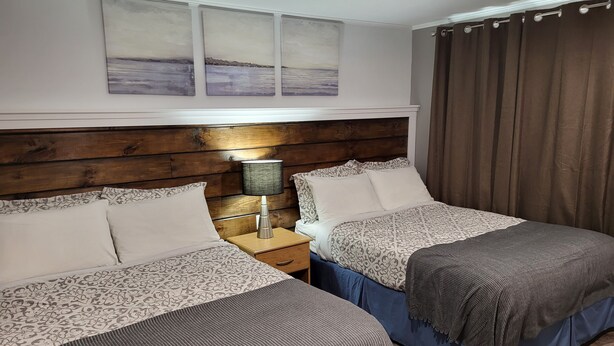 Een hotelkamer met twee bedden, een houten hoofdbord, een nachtkastje met een lamp, en uitzicht op zee vanuit het raam.