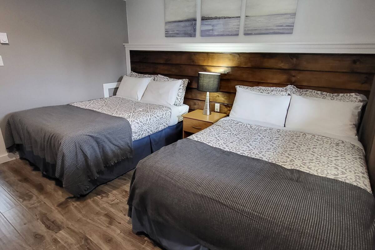 Una habitació d'hotel amb dos llits, sòl de fusta, una taula de nit amb una làmpada i un capçal de llit amb obra d'art.