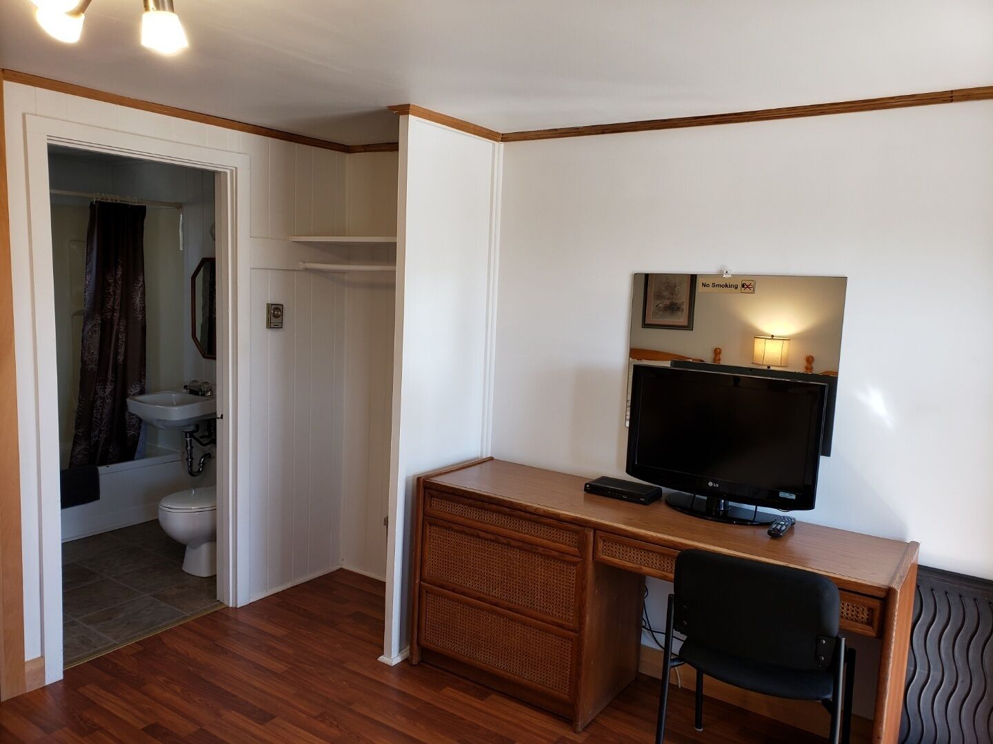Una habitación con un escritorio de madera, televisor, silla, baño con inodoro y lavamanos, y un cartel de 'No Fumar' en la pared.