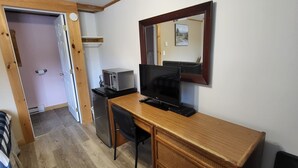 Een kleine kamer met een houten bureau, een televisie, een magnetron en een koelkast.