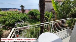 A private balcony with a view of a garden, a palm tree, and a building in the background. - BITINADA One-Bedroom Apartment (Rovinj)
