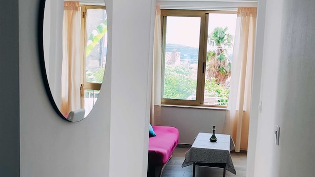 A narrow hallway with a bed, a table, and a window with curtains. - BITINADA One-Bedroom Apartment (Rovinj)
