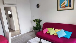 A living room with a red sofa, a small table, a potted plant, and a framed picture on the wall. - BITINADA One-Bedroom Apartment (Rovinj)