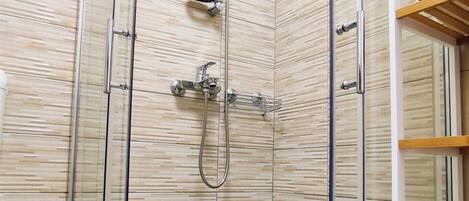 A glass-enclosed shower with a handheld showerhead and a wall-mounted faucet.