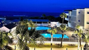 Zona de piscina con palmeras, vista al océano y un edificio con balcones.