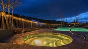 A hot tub area with a pool, surrounded by a wooden fence and trees, under evening sky. - Red Hawk Townhomes 2 Bedroom Rental in River Run Village (Keystone)