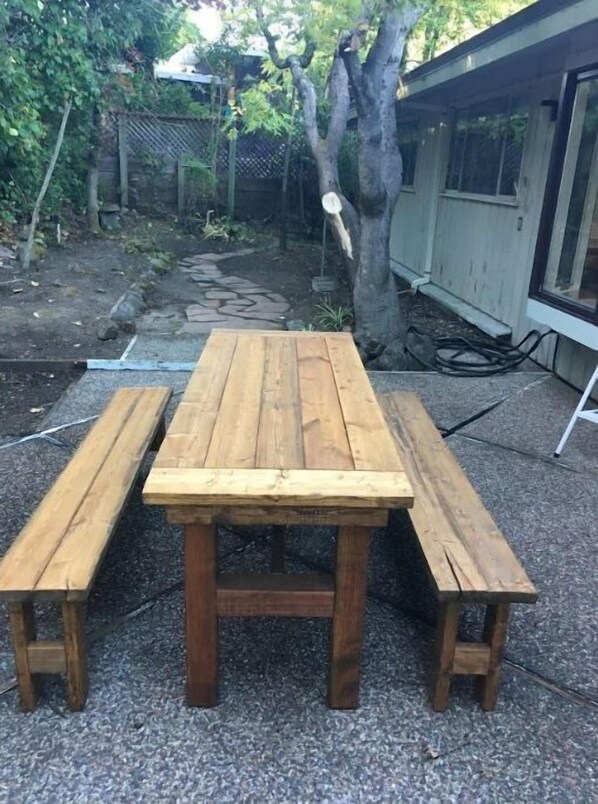 Enjoy a meal al fresco at this garden table, situated in front of a charming building with a window.