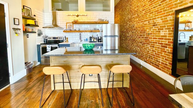 Una cocina moderna con una isla central, taburetes de bar y una pared de ladrillo decorativa.