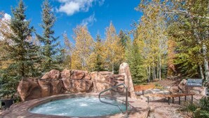 A hot tub surrounded by a rocky landscape with benches and a wooden deck.
