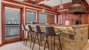 A kitchen with a stone island, bar stools, wooden cabinets, and a large range hood. - Exclusive 4 Bedroom Ski in, Ski out Vacation Rental With Hot Tubs and Heated Outdoor Pool in Lionshead Village (Vail)